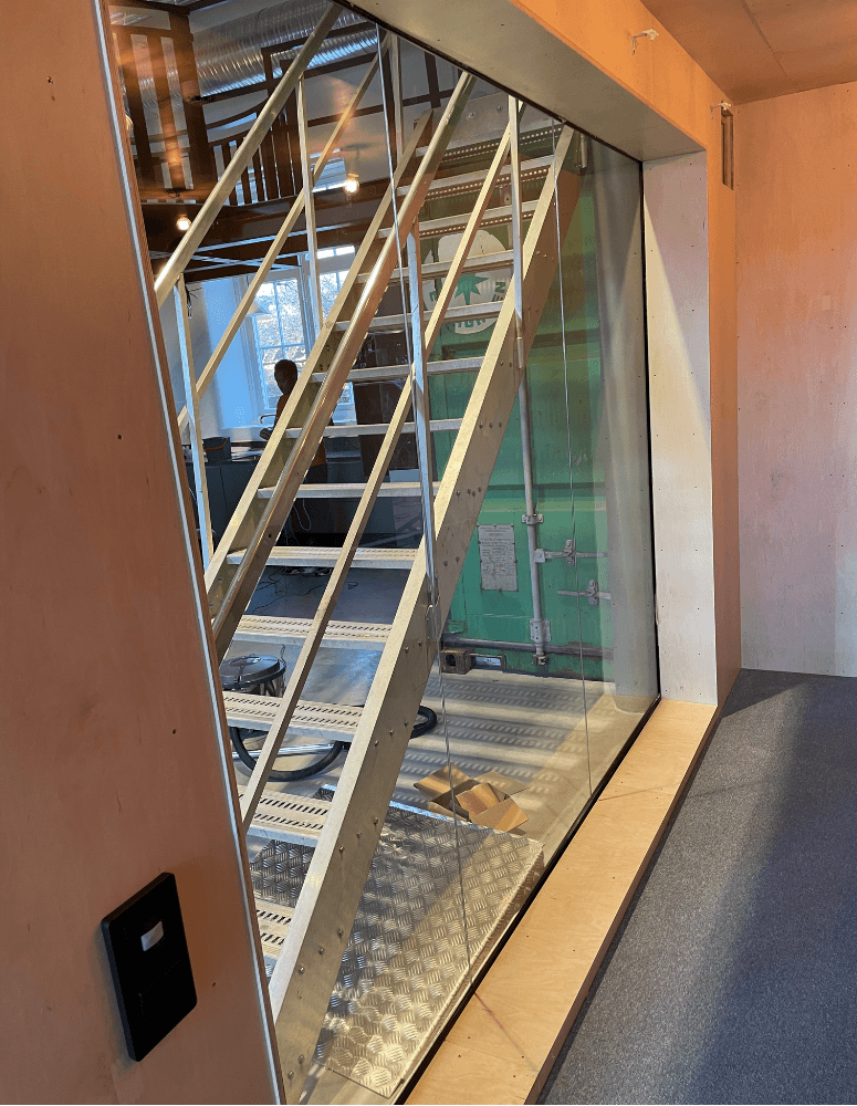 Ståltrappa och glasvägg installeras i containerdel – en del av kontorsanpassningen som kombinerar industriell design med transparens.
