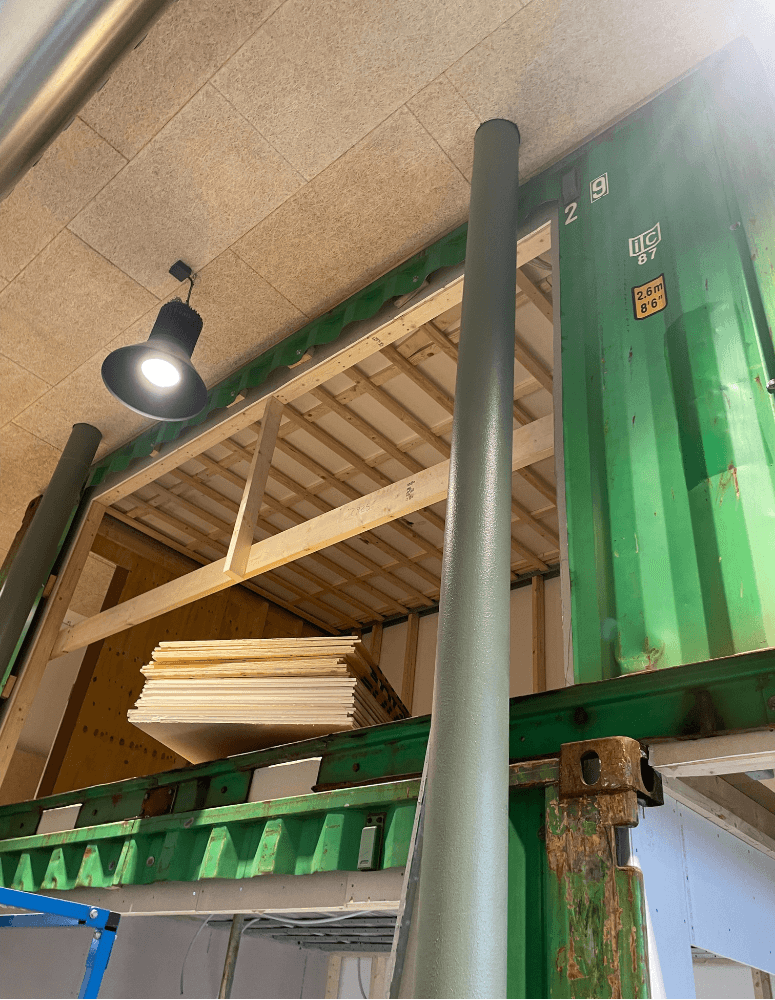 Inbyggd container med synligt bjälklag och byggmaterial – visar arbetet med att skapa ett stabilt entresolplan i kontorsmiljö.